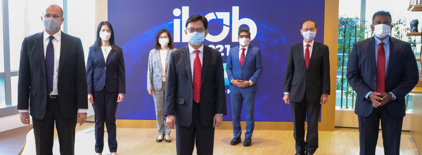 Seven masked professionals in business attire pose in front of a backdrop with "ILAB" on it.